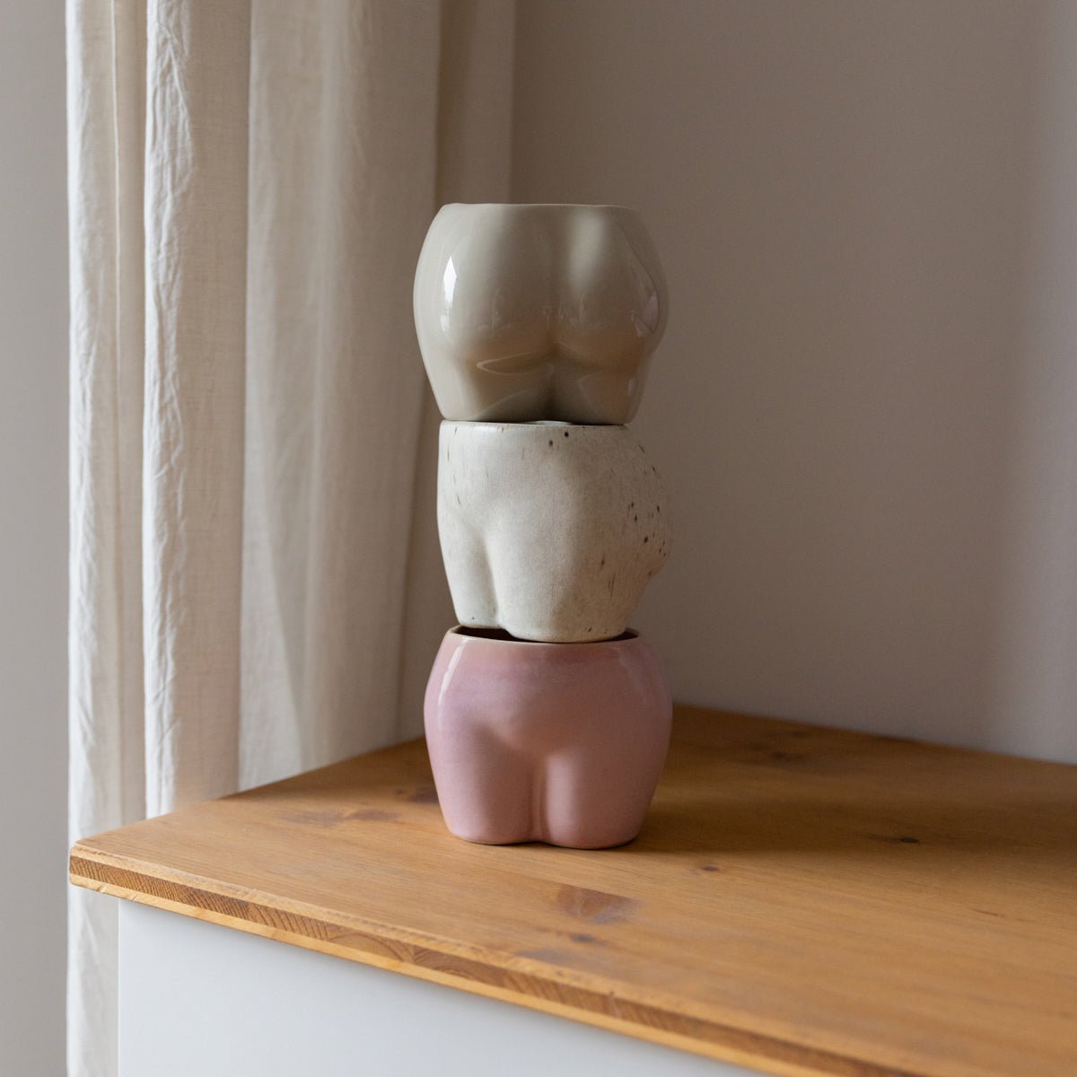 handgefertigte Body Becher aus Keramik in Natur, Rosa und Freckles von Studio Amun gestapelt auf einem Holzregal